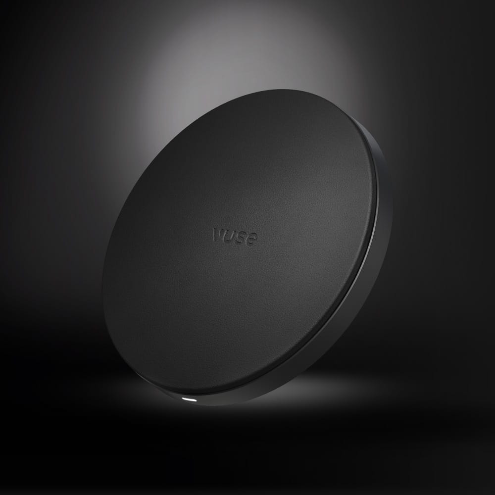 The Vuse Ultra Wireless Charger is a round, black pad with a smooth surface and "VUSE" embossed at the center, designed by Vuse for hassle-free charging. It’s shown against a dark gradient background.
