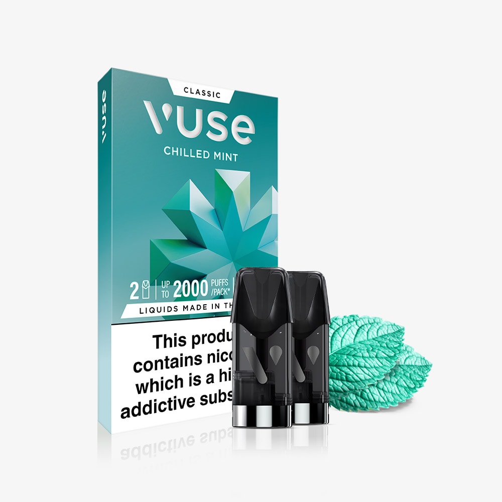 A Chilled Mint Vuse Classic Flavour Pods pack stands upright in a teal box with mint leaf designs. In front are two black pods and mint leaves, emphasizing the classic mint flavor and smooth nicotine salts blend.